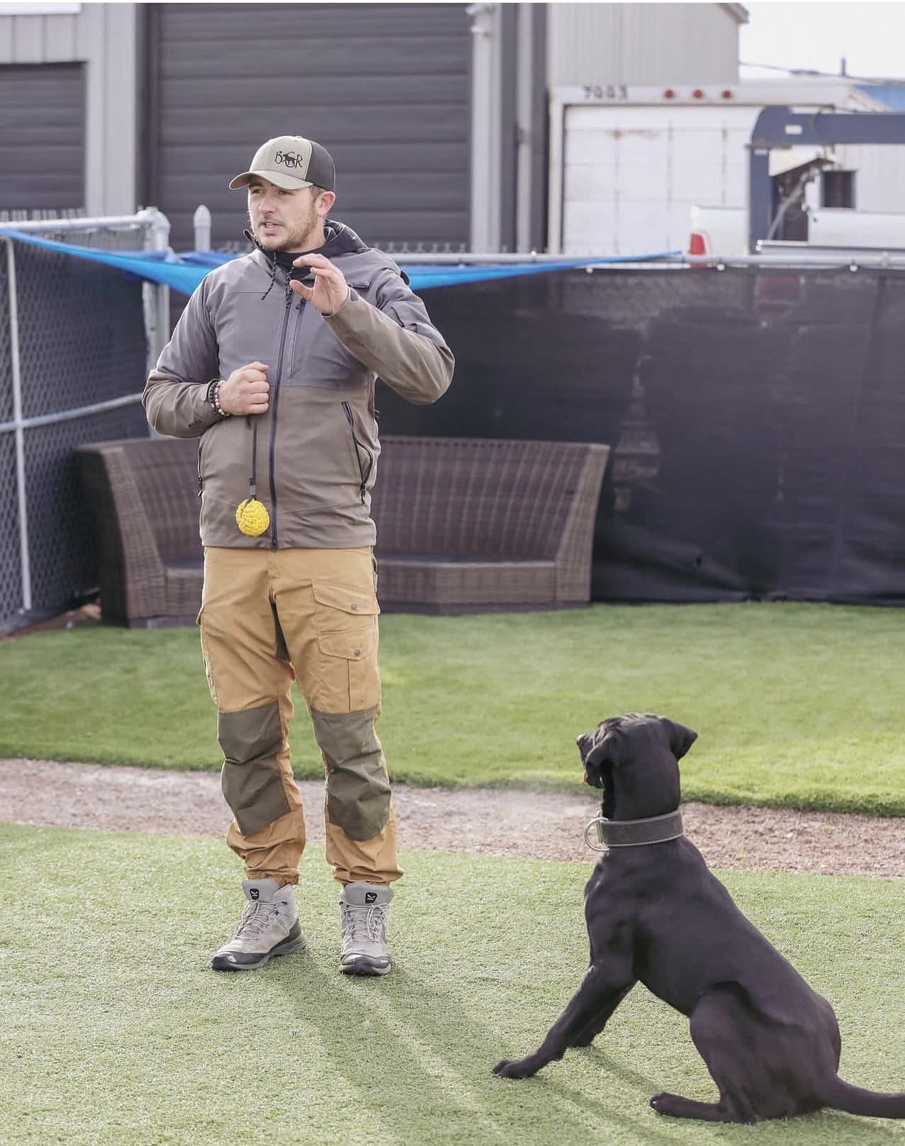 A dog trainer demonstrates a training topic while a black dog sits at attention